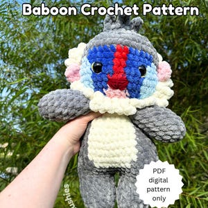 May include: A crocheted baboon plush toy with gray, white, blue, and red fur. The toy is being held in a hand with a green leafy background. The text "Baboon Crochet Pattern" is at the top of the image. A white circle with black text says "PDF digital pattern only".