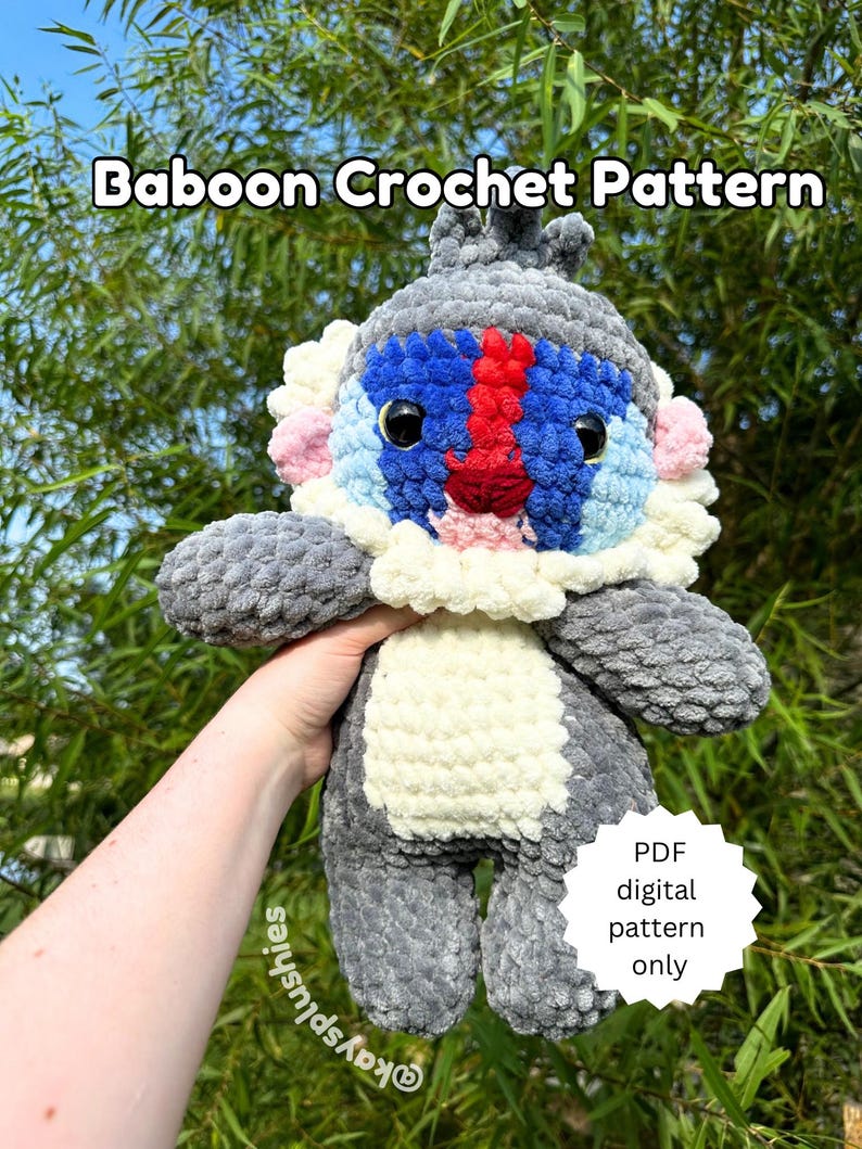 May include: A crocheted baboon plush toy with gray, white, blue, and red fur. The toy is being held in a hand with a green leafy background. The text "Baboon Crochet Pattern" is at the top of the image. A white circle with black text says "PDF digital pattern only".