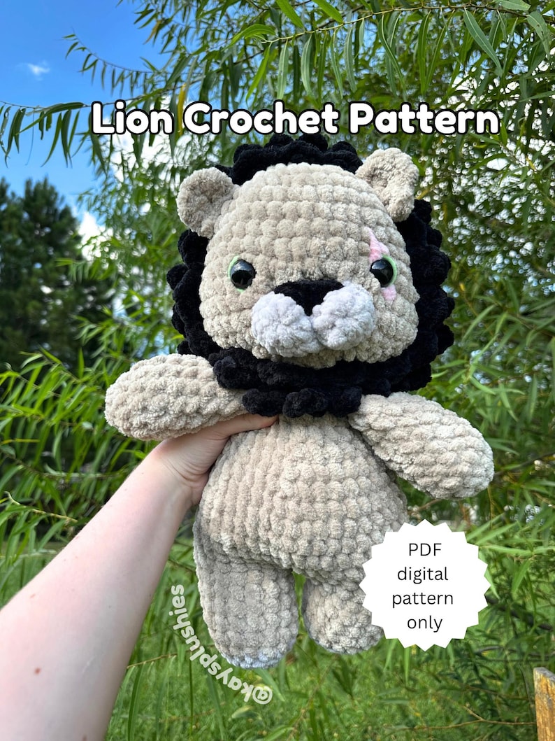 May include: A crocheted lion plush toy with black fur around its head and face. The lion has a white muzzle and pink nose. The toy is being held by a hand. The text "Lion Crochet Pattern" is at the top of the image. A white circle with the text "PDF digital pattern only" is in the lower right corner of the image.