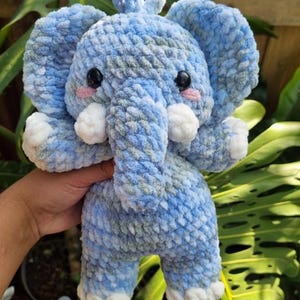 May include: A blue and green crocheted elephant plush toy with white accents. The elephant has a long trunk and big, round eyes.