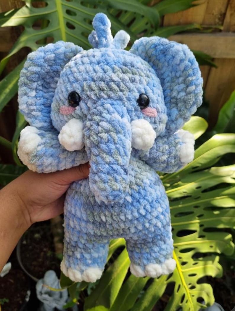 May include: A blue and green crocheted elephant plush toy with white accents. The elephant has a long trunk and big, round eyes.