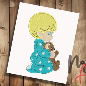 Puede incluir: Diseño bordado de un niño rubio con pijama azul que sostiene un oso de peluche marrón. El niño tiene una expresión dulce y mira al oso.