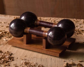 May include: A set of two wooden maracas with dark brown wooden handles and black spherical ends. The maracas are displayed on a wooden stand.