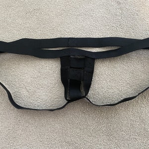 Op de afbeelding: Zwarte jockstrap met elastische tailleband en steunbandjes. De jockstrap heeft een zakje en een ontwerp met rugbandjes. Het materiaal lijkt een zachte, rekbare stof te zijn.