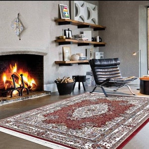 Puede incluir: Una alfombra de &aacute;rea roja, blanca y crema con un gran dise&ntilde;o floral intrincado en el centro. La alfombra est&aacute; colocada sobre un suelo de madera dura frente a una chimenea.