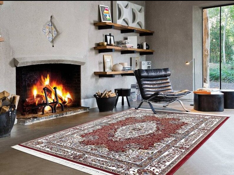 Puede incluir: Una alfombra de &aacute;rea roja, blanca y crema con un gran dise&ntilde;o floral intrincado en el centro. La alfombra est&aacute; colocada sobre un suelo de madera dura frente a una chimenea.