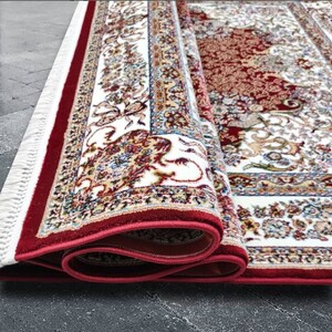 Puede incluir: Una alfombra roja y blanca con estampado y borde de flecos. La alfombra est&aacute; enrollada y los flecos son visibles.