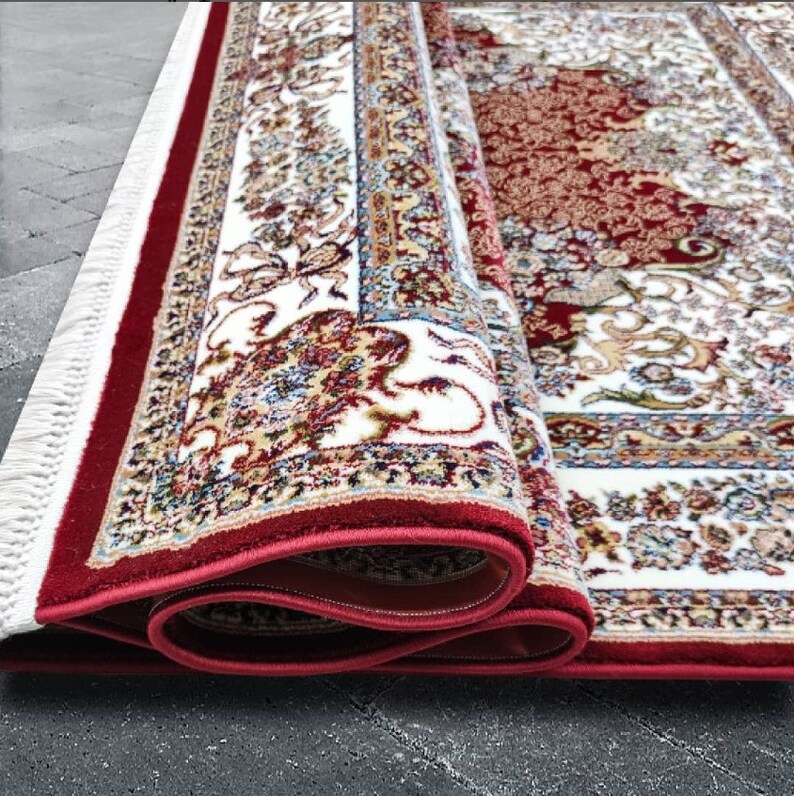 Puede incluir: Una alfombra roja y blanca con estampado y borde de flecos. La alfombra est&aacute; enrollada y los flecos son visibles.