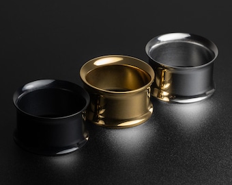 May include: Three ear gauges, one black, one gold, and one silver, are arranged in a row on a black surface.