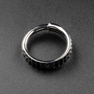 May include: A silver metal ring with a textured, triangular pattern around the entire circumference.