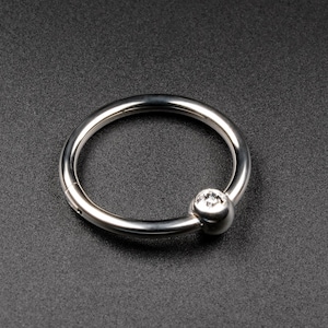 May include: A silver ring with a clear gem set in a round ball on the side.
