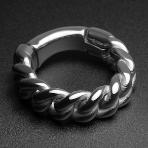 May include: A silver-colored ring with a thick, braided chain design. The ring has a smooth, polished finish and a solid, substantial appearance. The ring is a piece of jewelry.