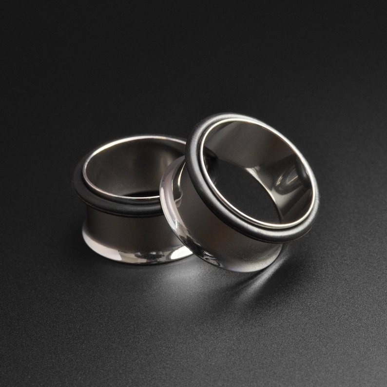May include: Two silver metal ear gauges with black rubber rings. The gauges are stacked on top of each other.