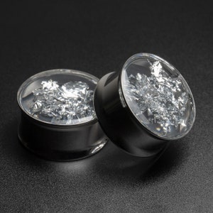 May include: Two silver ear gauges with a clear acrylic insert containing silver flakes. The gauges are made of stainless steel and have a polished finish.