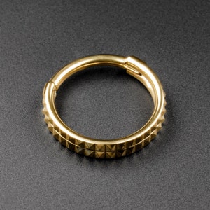 May include: A gold-colored metal ring with a textured, triangular pattern around the entire circumference.