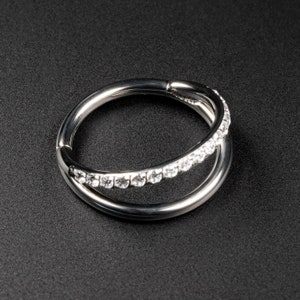 May include: A silver ring with a row of clear cubic zirconia stones set in a curved band. The ring is open and has a hinged clasp.