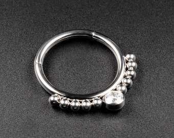 Könnte beinhalten: Ein silberner Ring mit einem klaren Edelstein und einer Reihe kleiner silberner Perlen.