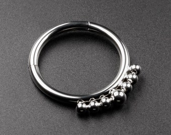 Könnte beinhalten: Ein silberner, runder Körperschmuck mit einer Reihe kleiner silberner Kugeln, die an der Unterseite hängen.