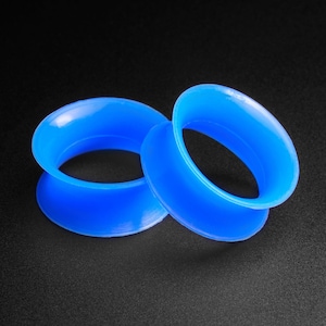 Peut inclure: Deux jauges d'oreille en silicone bleu, l'une légèrement plus grande que l'autre, sont présentées sur un fond noir.
