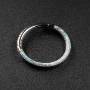May include: A silver ring with a white opal inlay. The ring is a seamless circle with a smooth, polished finish.