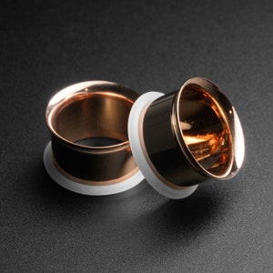 Puede incluir: Dos expansores de oreja de oro rosa con insertos de plástico blanco. Los expansores son redondos y tienen un acabado liso y pulido.