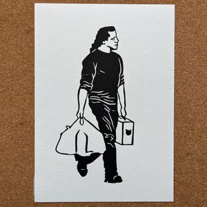 May include: Black and white linocut print of a person walking, carrying a bag and a box. The person is wearing a long-sleeved shirt and pants. The print is on white paper, set against a brown background.