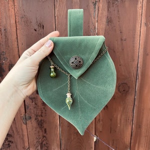 May include: A green velvet pouch shaped like a leaf with a metal clasp and a chain with two small glass vials hanging from it.