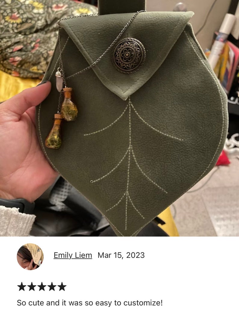 May include: A green leaf-shaped pouch with a silver chain and a decorative metal button. The pouch has a white stitching design and is made of leather.