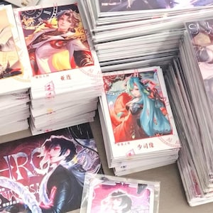 以下が含まれることがあります： アニメスタイルのキャラクターイラストが描かれた長方形のトレーディングカードのコレクション。カードは複数の山に積み重ねられており、カラフルな髪と詳細な衣装を持つ様々な人物が描かれ、中国語の文字が記されています。