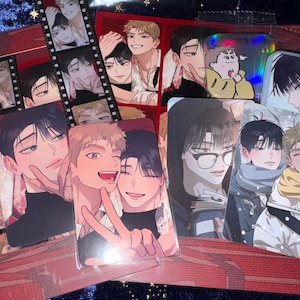 May include: A selection of anime-style character art cards depicting male figures. The cards display diverse poses and expressions, with a focus on soft colour palettes and detailed facial features. Some cards have a holographic finish.