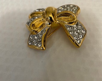 May include: A gold-tone bow brooch with clear rhinestones. The bow is made of metal and has a shiny finish.