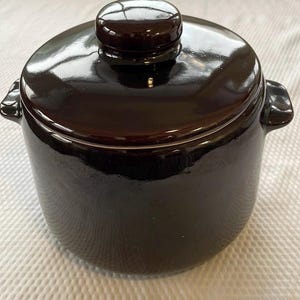 May include: A black ceramic crock pot with a lid. The crock pot has a white rim around the top.