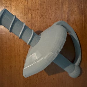 May include: A gray plastic toy shaped like a sword with a handle that has a textured surface.