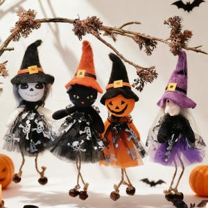 May include: Four hanging Halloween ornaments featuring a skeleton, a black cat, a pumpkin, and a witch, each wearing a pointed hat and a tulle skirt with skull patterns. The figures have dangling string legs with small dark bells at the feet.