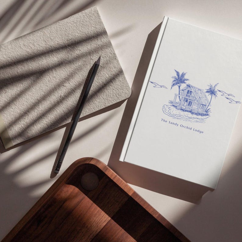 May include: A wooden serving tray, a gray notebook, a black pencil, and a white book with a blue illustration of a beach house and the text "The Sandy Orchid Lodge". The items are arranged on a light-colored surface.