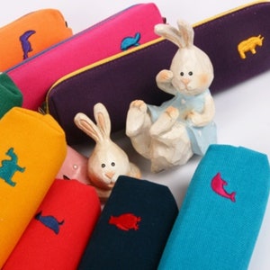 May include: Assortment of colorful pencil cases with embroidered animal designs. The cases are made of canvas and have a zipper closure.