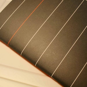 May include: A black notebook with white lines and a red line running diagonally across the cover.
