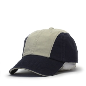 May include: A two-tone baseball cap with a beige crown and a navy blue brim and back. The cap has a curved brim and a structured crown.