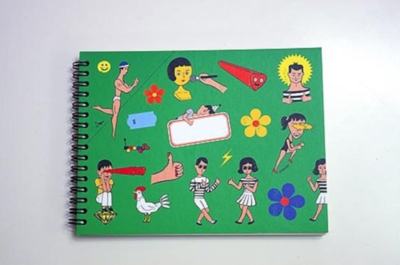 May include: A green spiral bound notebook with colorful illustrations of people, flowers, and geometric shapes. The notebook has a blank white rectangle in the center.