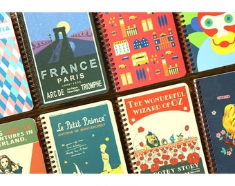 May include: A collection of colorful spiral bound notebooks with various designs. The notebooks feature illustrations of the Eiffel Tower, a bus, a monkey, a bird, and a lion. The covers also include text such as "France Paris", "The Wonderful Wizard of Oz", and "Le Petit Prince".