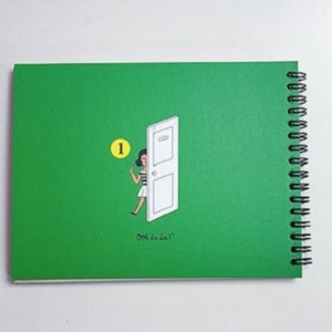 May include: A green spiral bound notebook with a white door and a woman in a white dress and black hair peeking out. The number "1" is circled in yellow. The text "ooh la la" is printed on the cover.