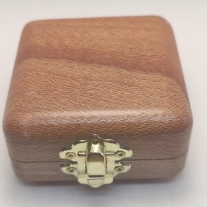May include: A small, wooden box with a gold latch. The box has a light brown wood grain pattern.