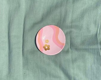 May include: A pink and white ceramic dish with a wavy design and gold flower accents. The dish is perfect for holding jewelry or other small items.