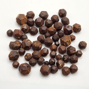 Könnte beinhalten: Eine Sammlung brauner, dodekaedrischer Pyritkristalle. Die Kristalle sind in verschiedenen Größen und haben einen metallischen Glanz.