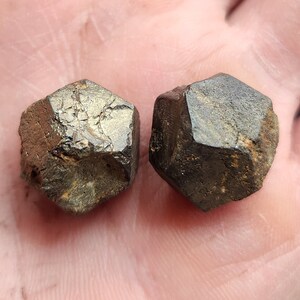 Könnte beinhalten: Zwei dunkelbraune, facettierte, geometrische Kristalle mit einem metallischen Glanz.