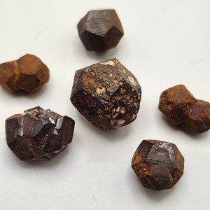 Könnte beinhalten: Sechs braune und schwarze Pyritkristalle, einige mit rauer Textur und andere mit glatter, facettierter Oberfläche.