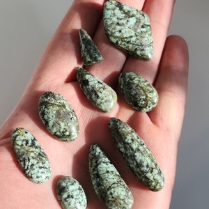 Könnte beinhalten: Eine Sammlung von neun Türkis-Cabochons in verschiedenen Formen und Größen. Die Steine sind in einem gemusterten Grün und Braun mit einer glatten, polierten Oberfläche.