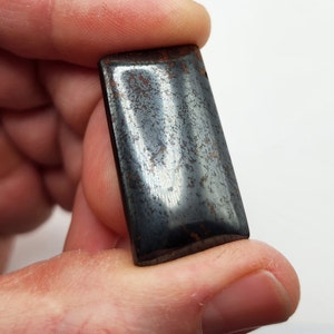 Könnte beinhalten: Ein rechteckiger Edelstein in Dunkelgrau und Braun mit einer glatten, polierten Oberfläche.