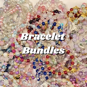 May include: A collection of colorful beaded bracelets in various shades of pink, purple, blue, and clear. The bracelets are made with different types of beads and charms. The text "Bracelet Bundles" is displayed in white letters with a black outline.