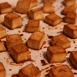 May include: A baking tray lined with baking parchment and filled with golden brown tofu cubes.